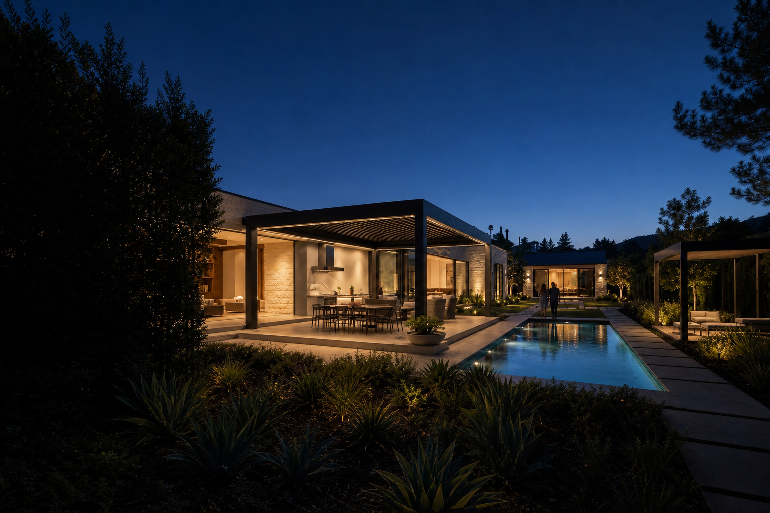 A calm California property at blue hour with outdoor rooms and an independent residence illuminated across the landscape